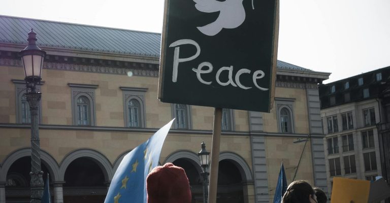 A crowd in Munich holds a peace sign during a peaceful protest in the city square.