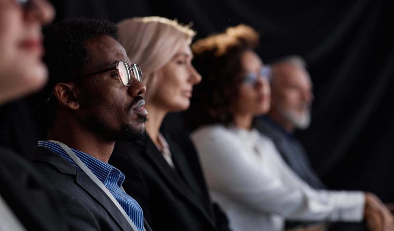 Side view of Black male finance executive wearing glasses sitting in row with colleagues while attending leadership conference in auditorium, copy space